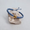 pulsera cruz azul, hecha a mano con poliéster encerado y una pieza con baño de oro en el centro. Cierre ajustable mediante nudo corredero